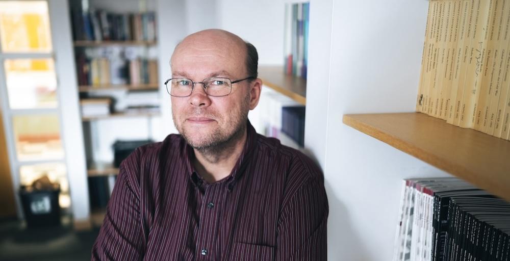 Jeremy Littau poses for a portrait in his office and lends against a book shelf.